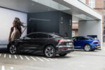 Deux Audi électriques stationnées sous l’auvent d’une station de recharge, avec un câble branché sur la voiture au premier plan.