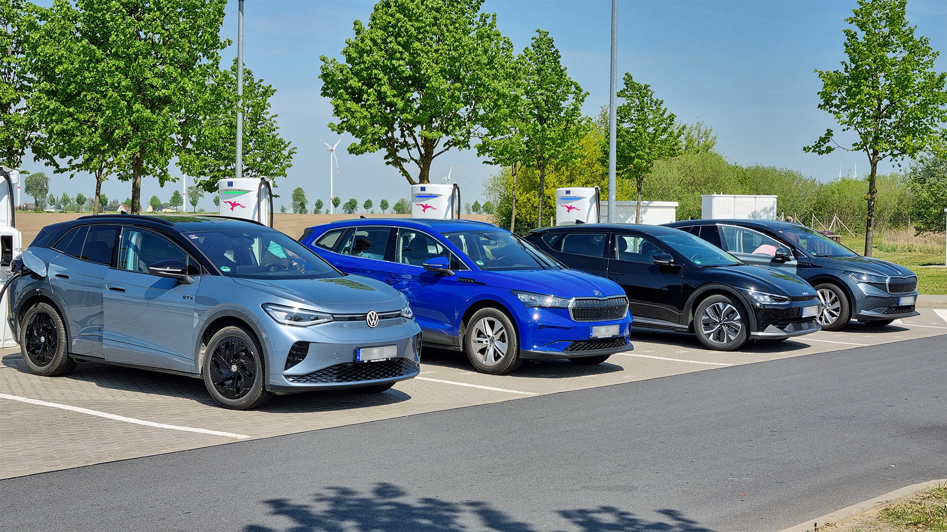 Quatre voitures électriques stationnées devant des bornes Ionity sur une aire arborée, par temps ensoleillé.