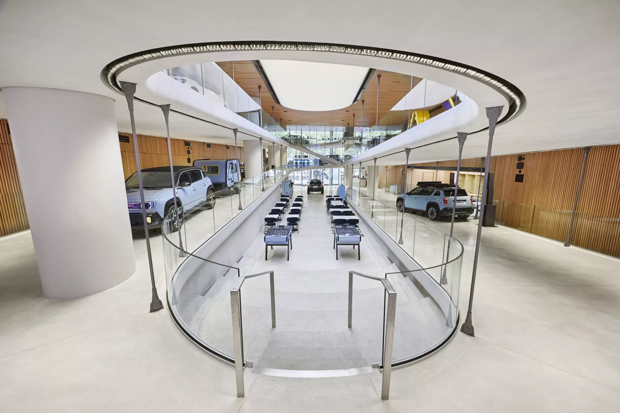 Vue d’ensemble d’un showroom Renault lumineux, avec plusieurs voitures exposées de part et d’autre d’un escalier central bordé de verre.